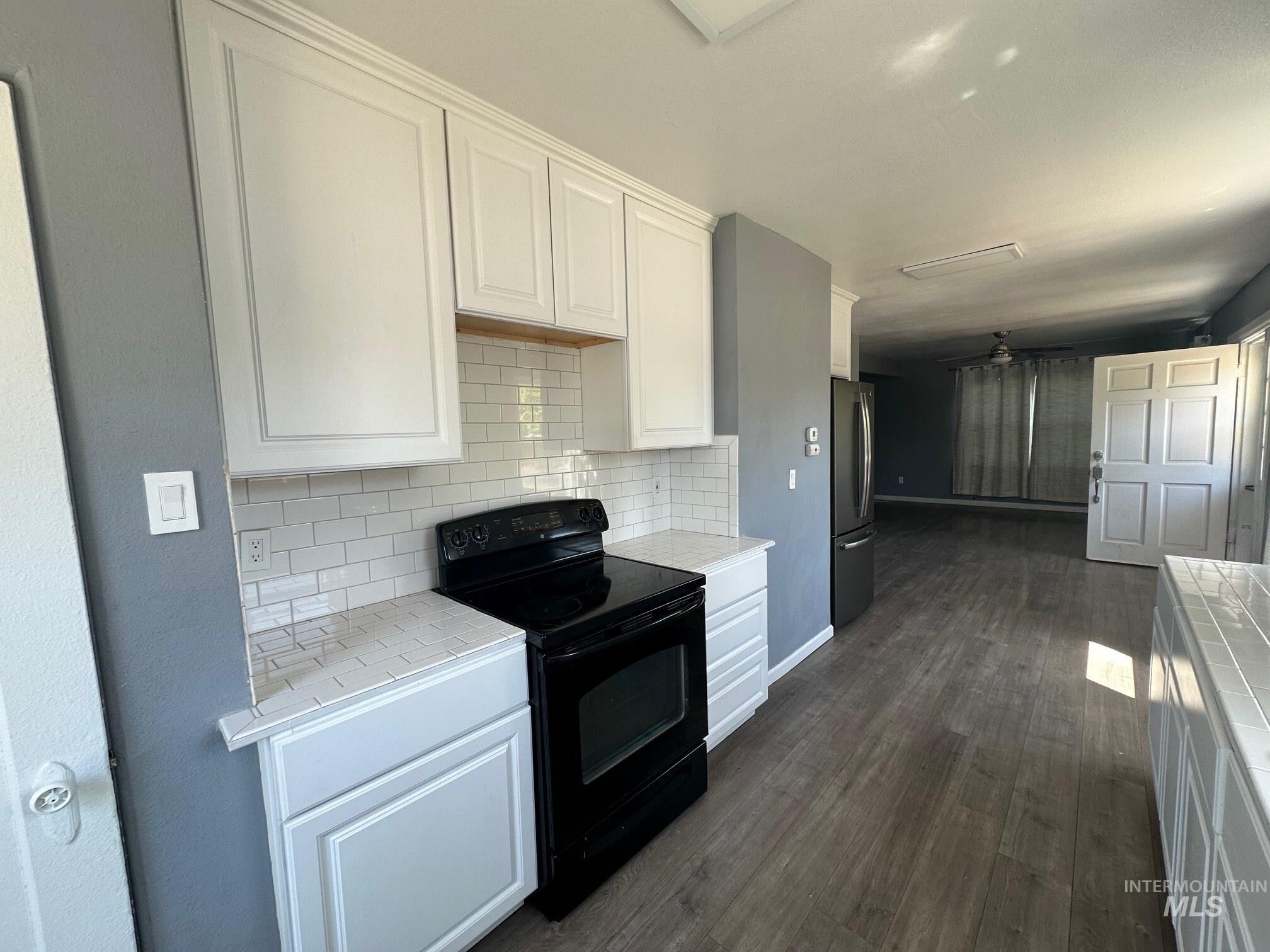 787 Southwest 3rd Street Ontario, OR 97914 - Photo 4 of 22 Kitchen featuring black / electric stove, tasteful backsplash, tile countertops, white cabinetry, and dark wood-style flooring