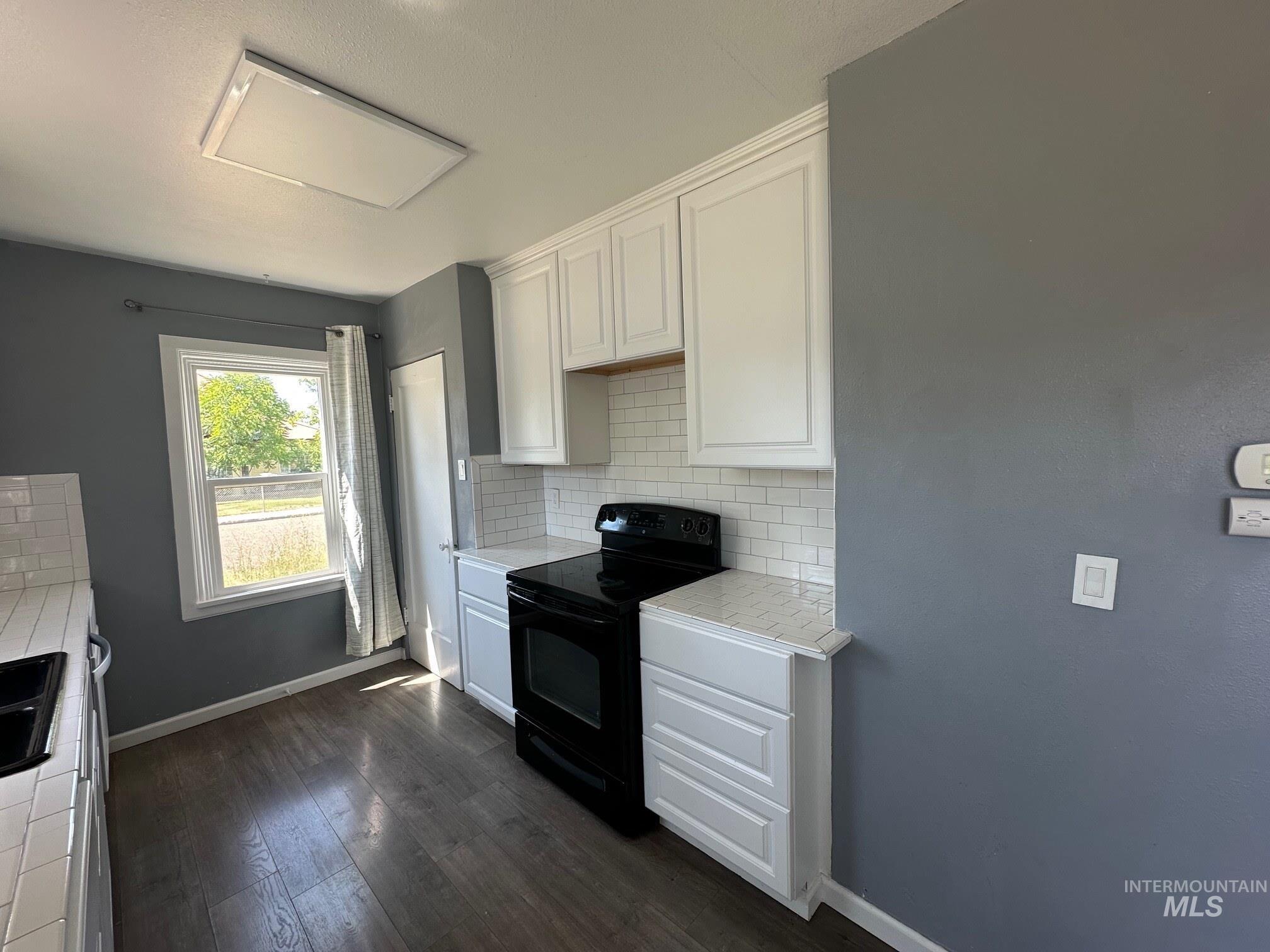 787 Southwest 3rd Street Ontario, OR 97914 - Photo 5 of 22 Kitchen with black range with electric cooktop, white cabinets, backsplash, and dark wood-style floors