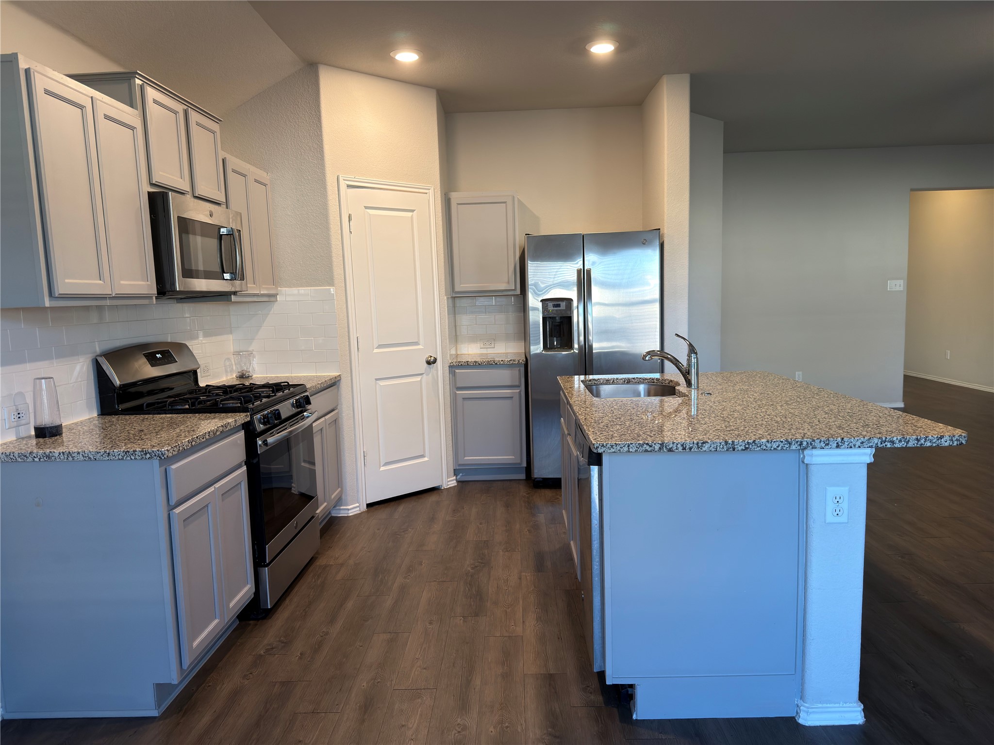 21700 Urraca Lane Pflugerville, TX 78660 - Photo 5 of 40 Kitchen with appliances with stainless steel finishes, light stone countertops, dark wood-style flooring, a kitchen island with sink, and backsplash
