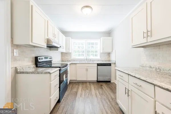 a kitchen with granite countertop white cabinets a sink dishwasher and a stove with wooden floor