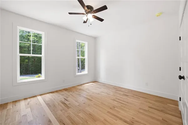an empty room with wooden floor ceiling fan and windows