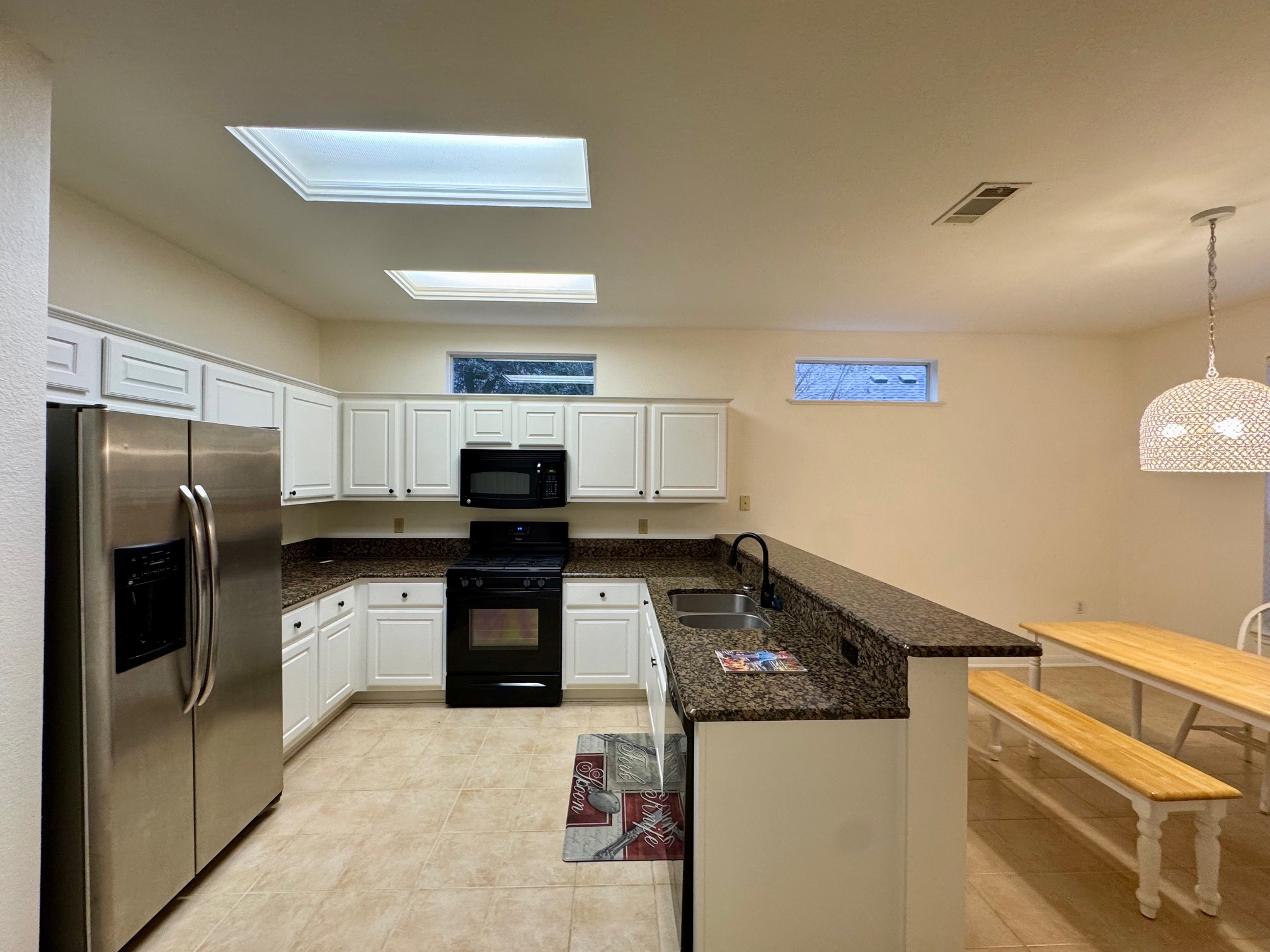 262 Whispering Wind Drive Georgetown, TX 78633 - Photo 2 of 20 Kitchen featuring a peninsula, black appliances, dark stone counters, white cabinets, and hanging light fixtures