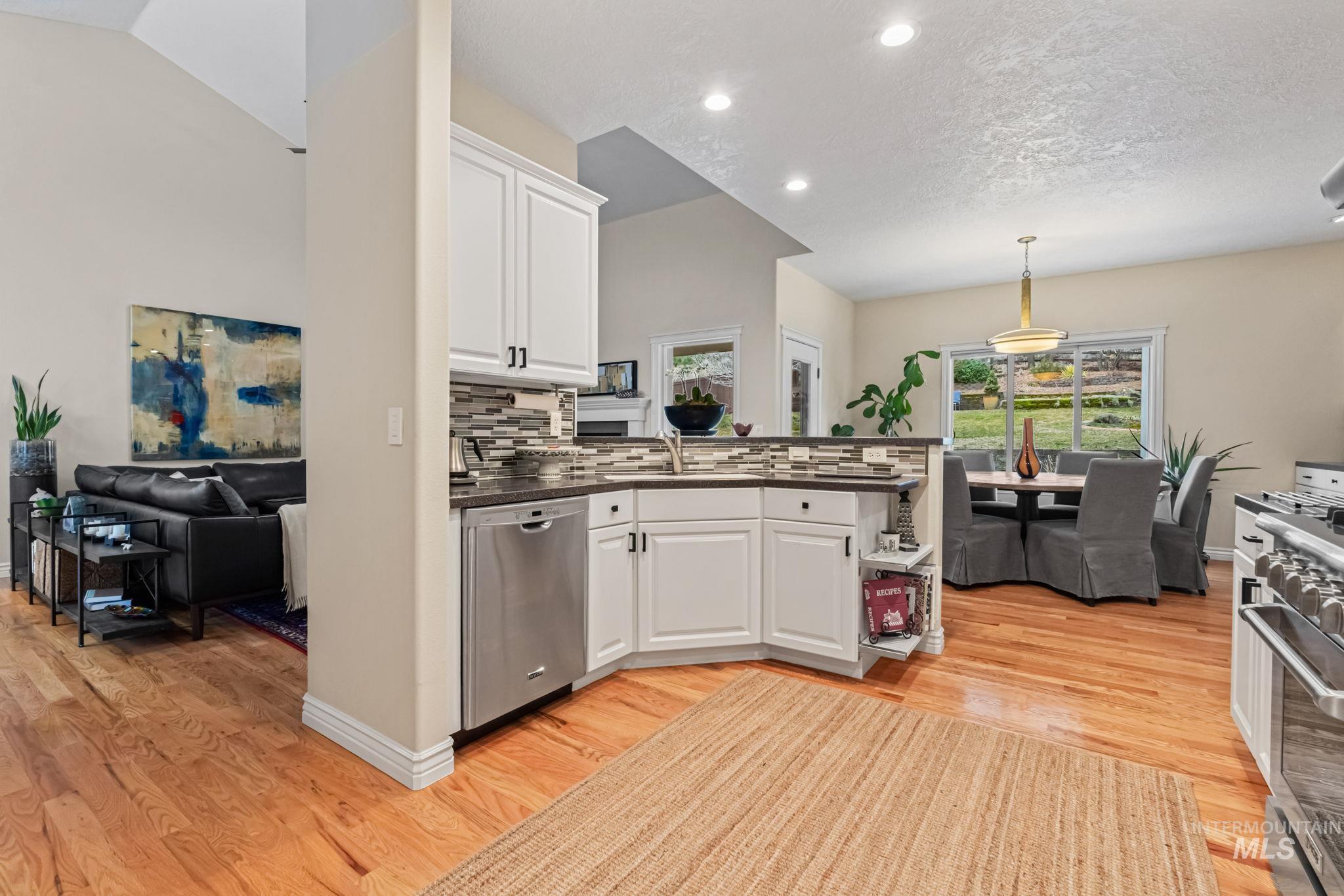 4235 Trekker Rim Drive East Boise, ID 83716 - Photo 11 of 33 Kitchen featuring white cabinetry, a peninsula, pendant lighting, appliances with stainless steel finishes, and decorative backsplash