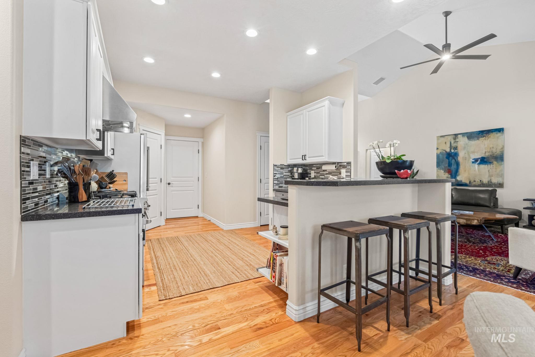 4235 Trekker Rim Drive East Boise, ID 83716 - Photo 9 of 33 Kitchen with white cabinets, a breakfast bar, light wood-style floors, decorative backsplash, and wall chimney exhaust hood