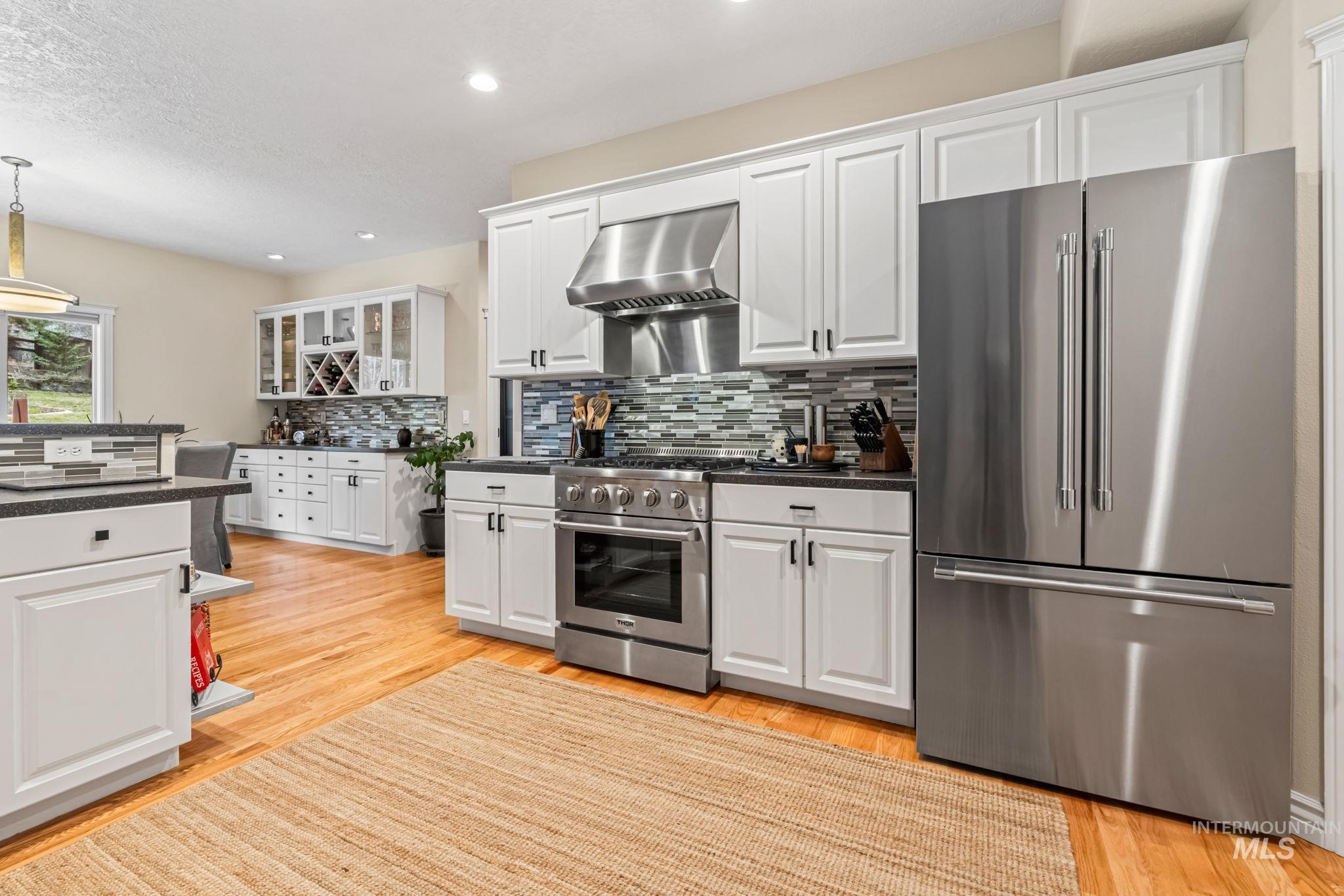 4235 Trekker Rim Drive East Boise, ID 83716 - Photo 10 of 33 Kitchen featuring premium appliances, white cabinets, light wood finished floors, wall chimney exhaust hood, and recessed lighting