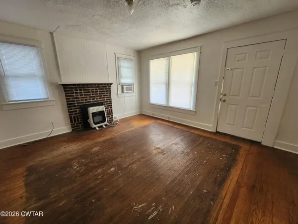 an empty room with wooden floor fireplace and windows