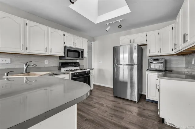 a kitchen with granite countertop a refrigerator a sink a stove a microwave and wooden floor