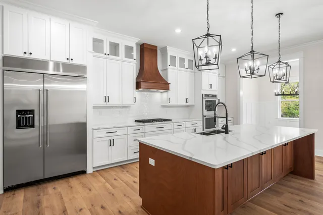 a kitchen with stainless steel appliances granite countertop a refrigerator a sink dishwasher a stove and white countertops with wooden floor