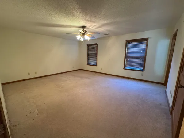 an empty room with a chandelier fan and windows