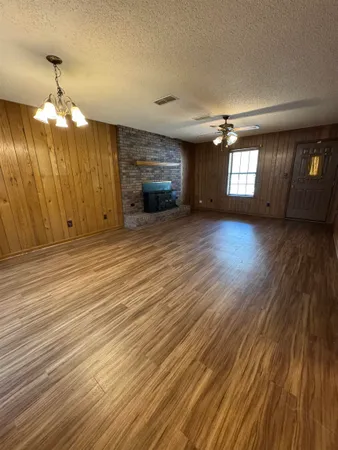 an empty room with wooden floor chandelier and windows