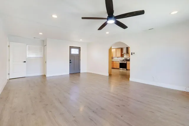 an empty room with wooden floor ceiling fan and windows