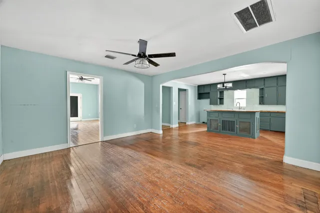 a view of an empty room with wooden floor and a ceiling fan