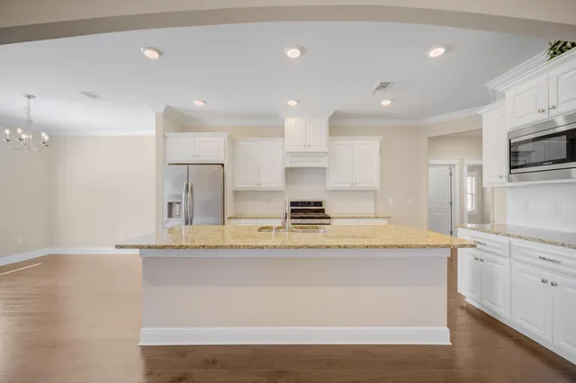 a large kitchen with stainless steel appliances granite countertop a stove a sink a refrigerator and white cabinets with wooden floor