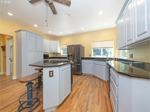 a kitchen with stainless steel appliances a refrigerator a sink dishwasher a stove top oven a dining table and chairs with wooden floor