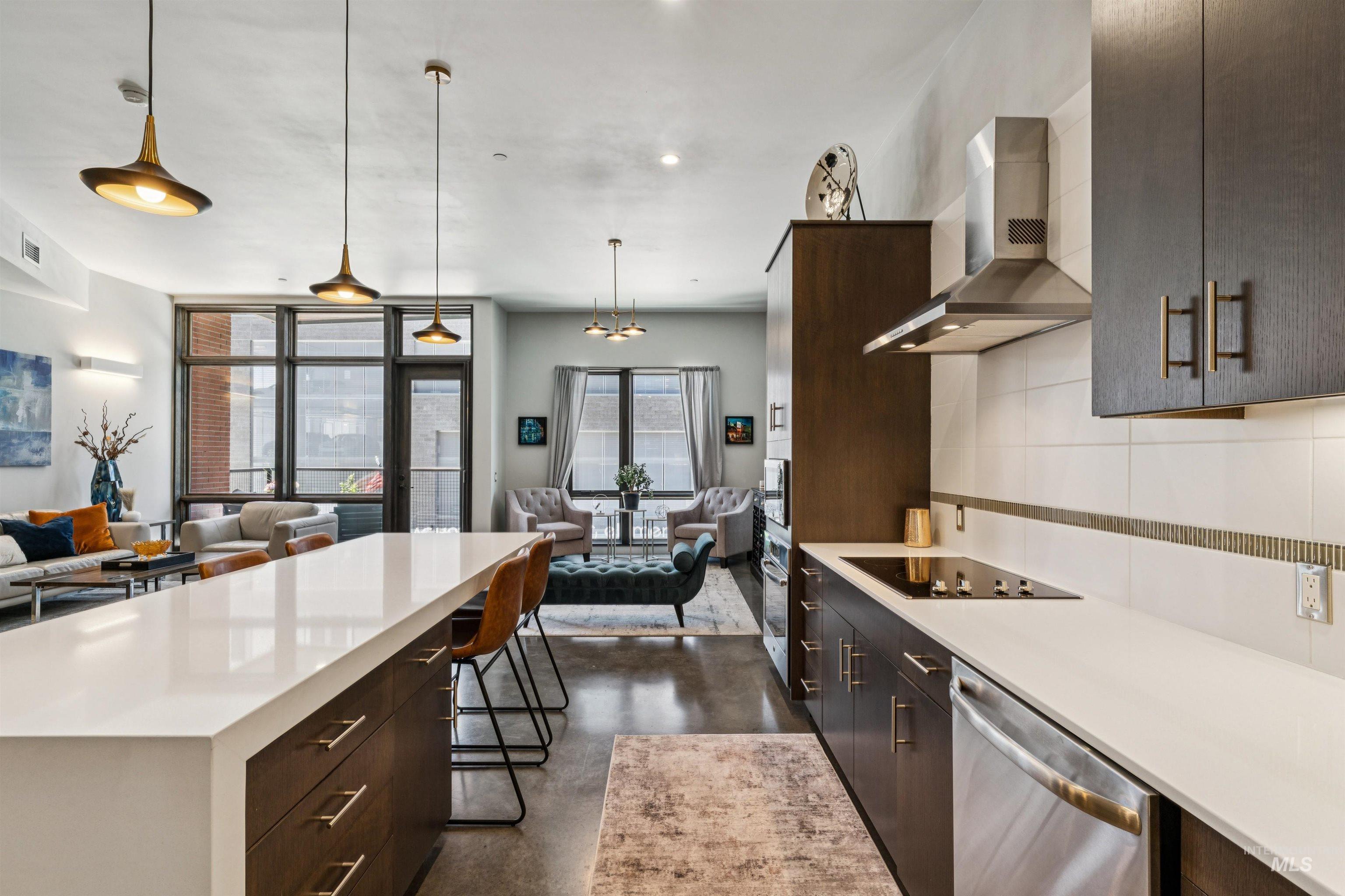 119 South 10th Street, Unit 307 Boise, ID 83702 - Photo 16 of 47 Open-concept kitchen featuring an expansive island with a waterfall countertop, dark wood-finish cabinetry, stainless steel appliances, and pendant lighting
