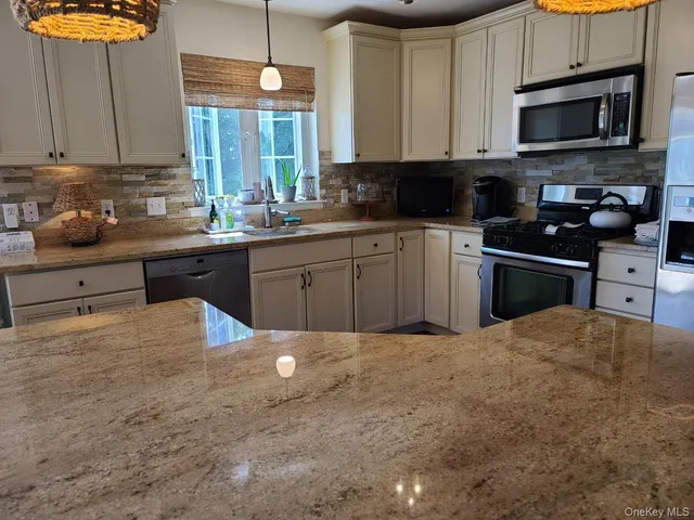 a kitchen with stainless steel appliances granite countertop a stove a sink dishwasher and a microwave oven with white cabinets