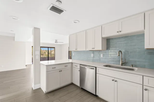 a kitchen with a sink dishwasher and white cabinets with wooden floor