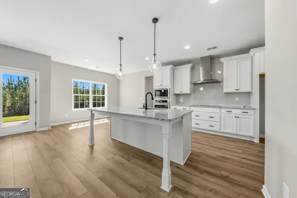 a large kitchen with granite countertop a stove a sink a refrigerator and white cabinets with wooden floor