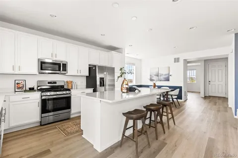 a kitchen with stainless steel appliances a microwave a stove a sink a refrigerator and white cabinets with wooden floor