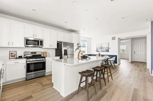 a kitchen with stainless steel appliances a microwave a stove a sink a refrigerator and white cabinets with wooden floor