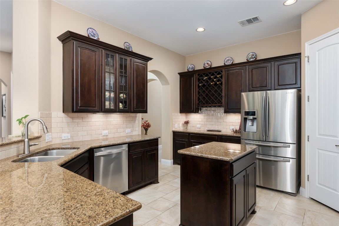 399 Whispering Wind Way Austin, TX 78737 - Photo 18 of 40 Kitchen featuring appliances with stainless steel finishes, arched walkways, dark brown cabinetry, light stone counters, and tasteful backsplash
