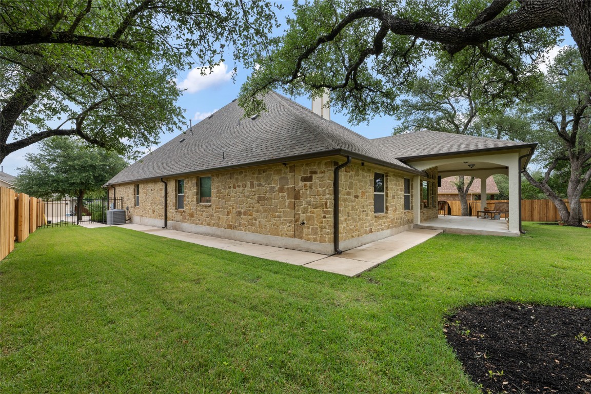 399 Whispering Wind Way Austin, TX 78737 - Photo 35 of 40 Rear view of property with a shingled roof, a patio, a chimney, a fenced backyard, and stone siding