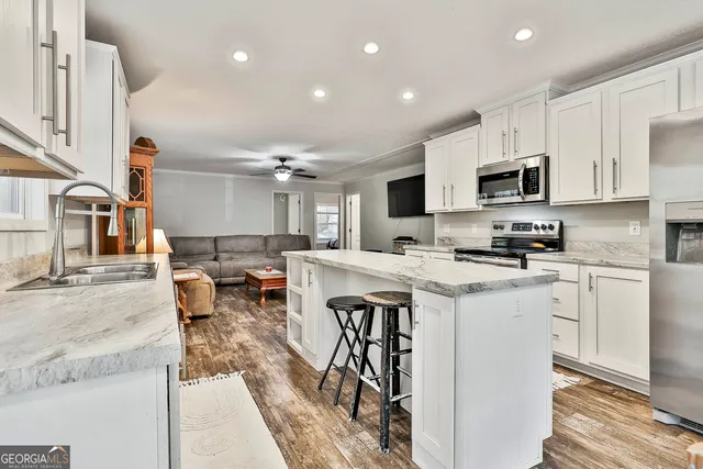 a kitchen with stainless steel appliances granite countertop a stove top oven a sink a refrigerator and white cabinets with wooden floor