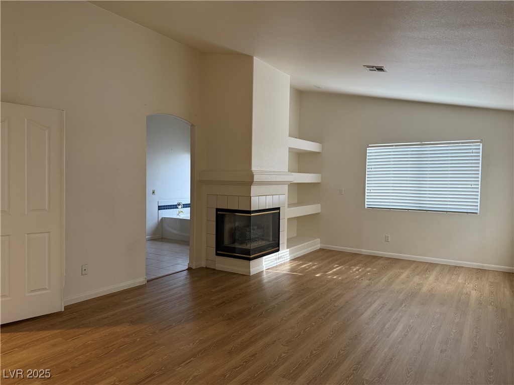 2733 Chokecherry Avenue Henderson, NV 89074 - Photo 16 of 26 Unfurnished living room featuring lofted ceiling, a tiled fireplace, arched walkways, light wood finished floors, and built in features