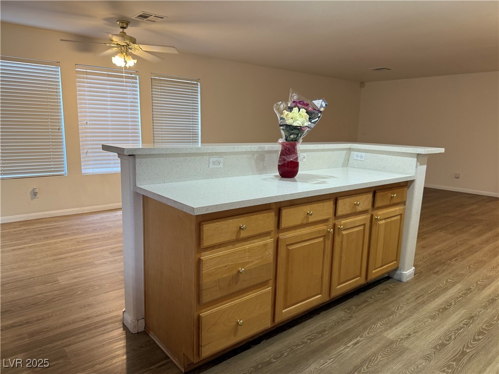 2733 Chokecherry Avenue Henderson, NV 89074 - Photo 6 of 26 Kitchen featuring brown cabinetry, a kitchen island, light wood finished floors, light stone countertops, and ceiling fan
