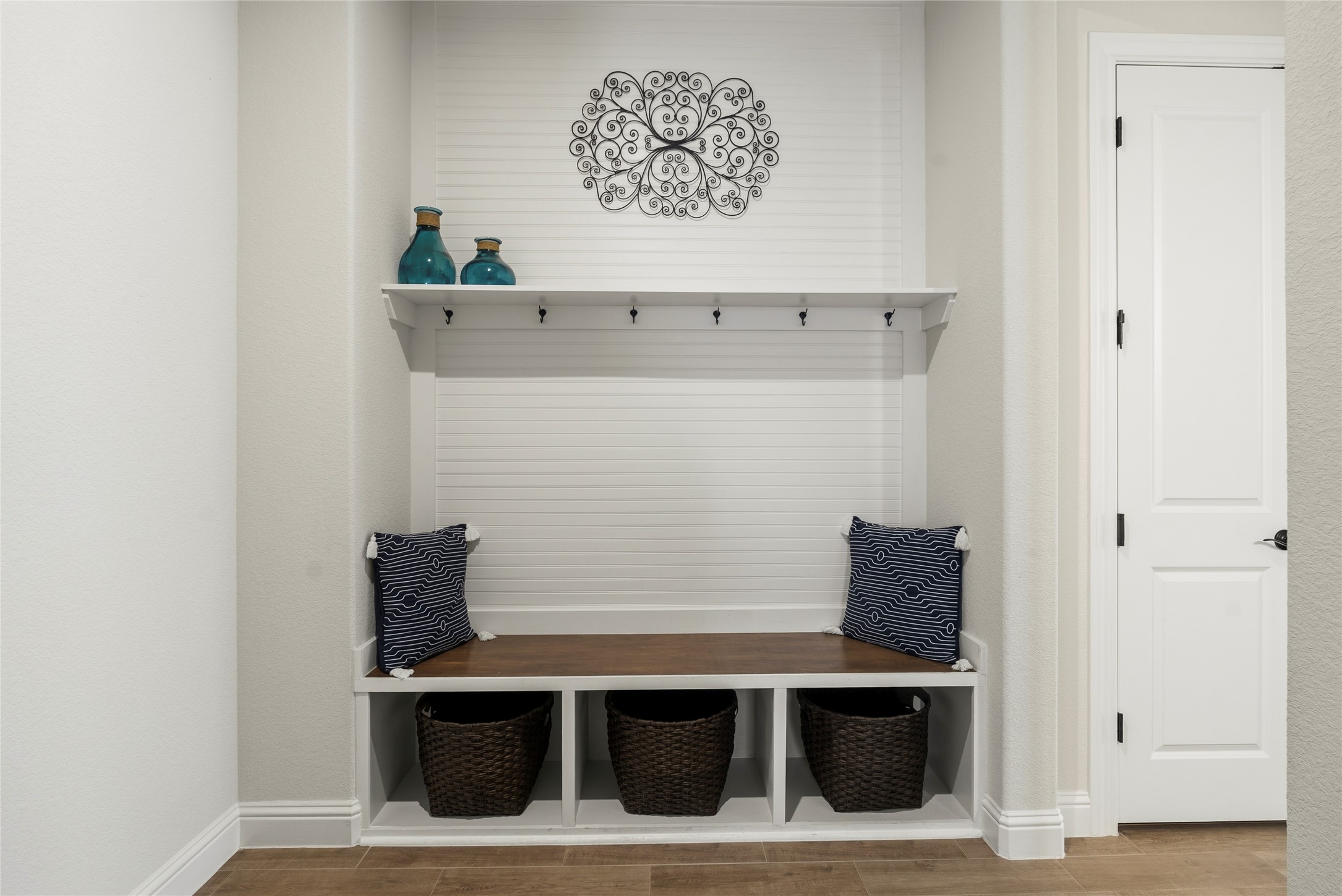 4513 Vieste View Leander, TX 78641 - Photo 9 of 40 Built-in mudroom bench featuring a wood-finish seat, three storage cubbies, a beadboard back panel, and an upper shelf with coat hooks