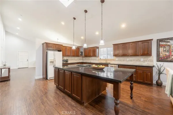 a kitchen with stainless steel appliances granite countertop a stove a sink a refrigerator and a wooden floor