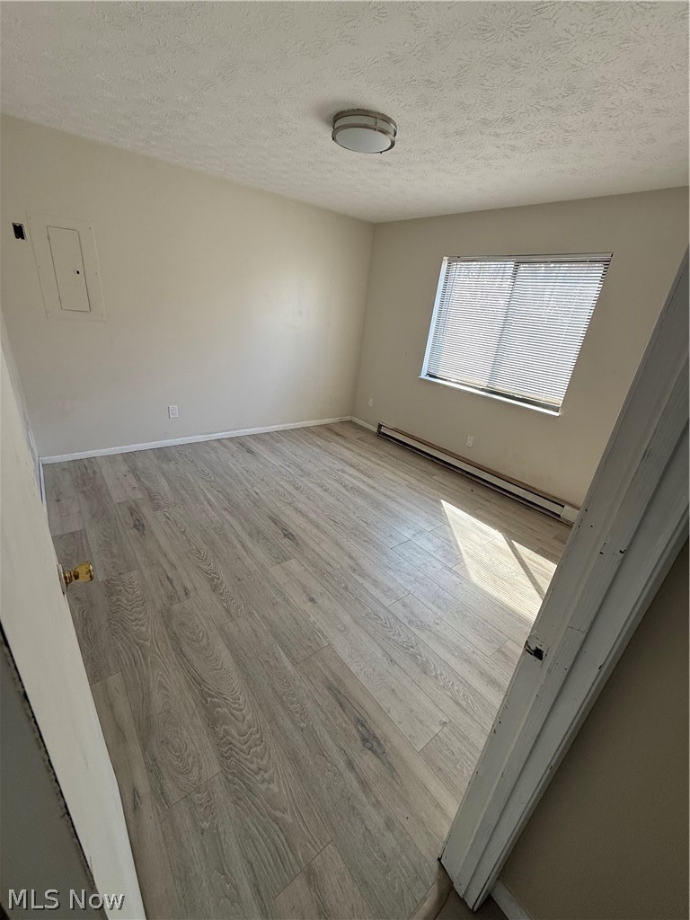 662 Sumner Street Akron, OH 44311 - Photo 6 of 10 Empty room featuring baseboard heating, light wood-style floors, a textured ceiling, and electric panel