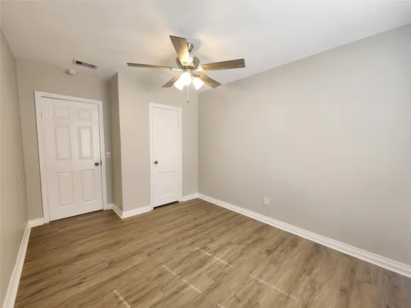 an empty room with wooden floor fan and windows