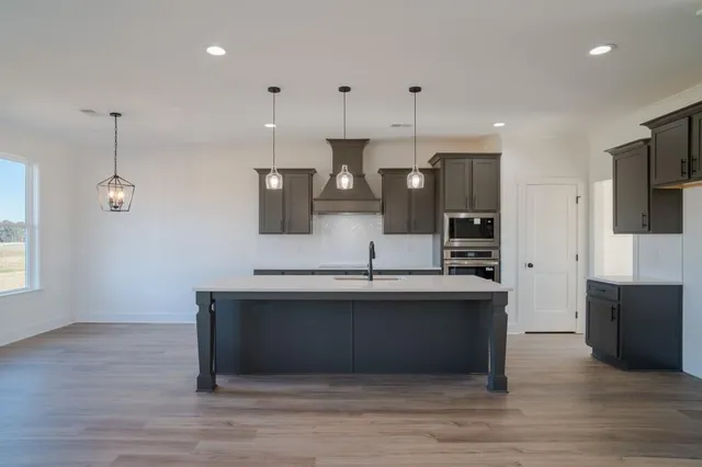 a large kitchen with stainless steel appliances granite countertop a sink a stove and a wooden floor