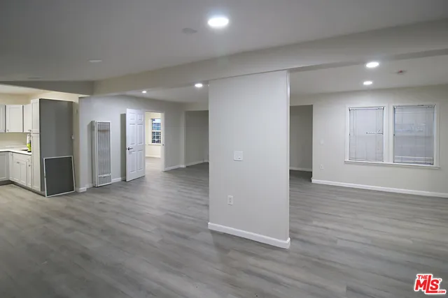 a view of an empty room with wooden floor and a kitchen