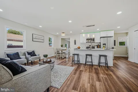 a living room with stainless steel appliances furniture wooden floor and a kitchen view