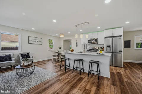 a living room with stainless steel appliances a dining table wooden floor and a view of kitchen
