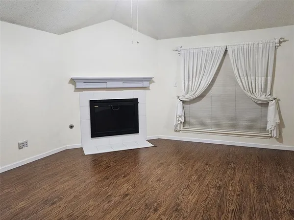 a view of an empty room with wooden floor and a fireplace