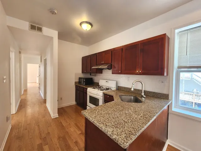 a kitchen with stainless steel appliances kitchen island granite countertop a stove top oven a sink dishwasher a refrigerator and a microwave oven with wooden floor