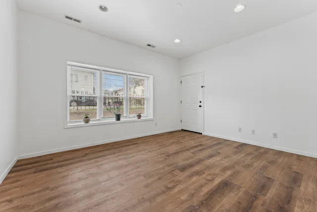 a view of an empty room with a window and wooden floor