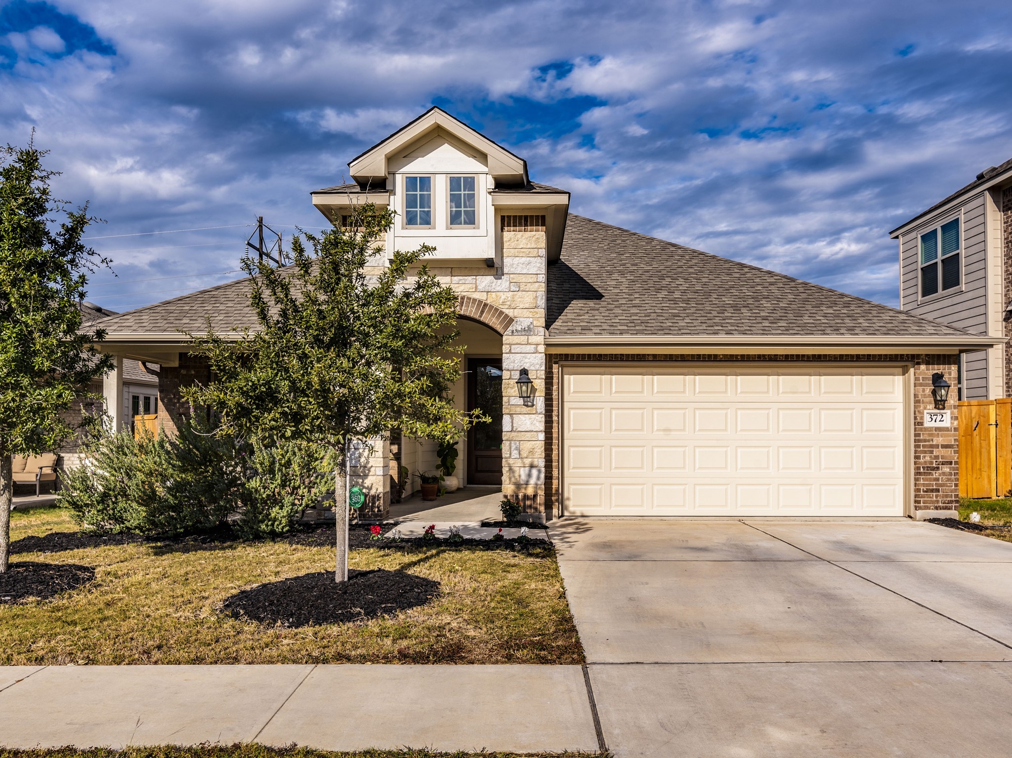 View of front of property featuring an attached garage, concrete driveway, stone siding, roof with shingles, and a front lawn