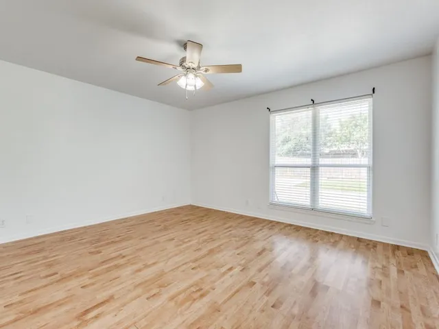 an empty room with wooden floor fan and windows