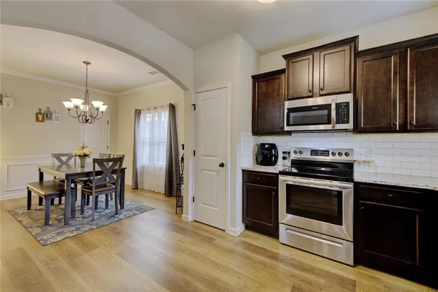 a kitchen with stainless steel appliances granite countertop a stove top oven a sink dishwasher a dining table and chairs with wooden floor