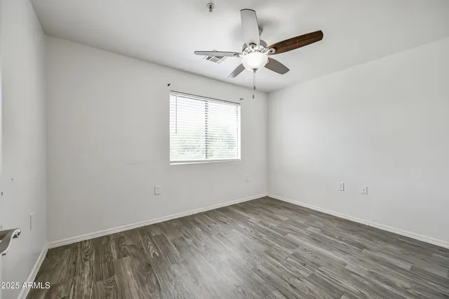 an empty room with wooden floor fan and windows