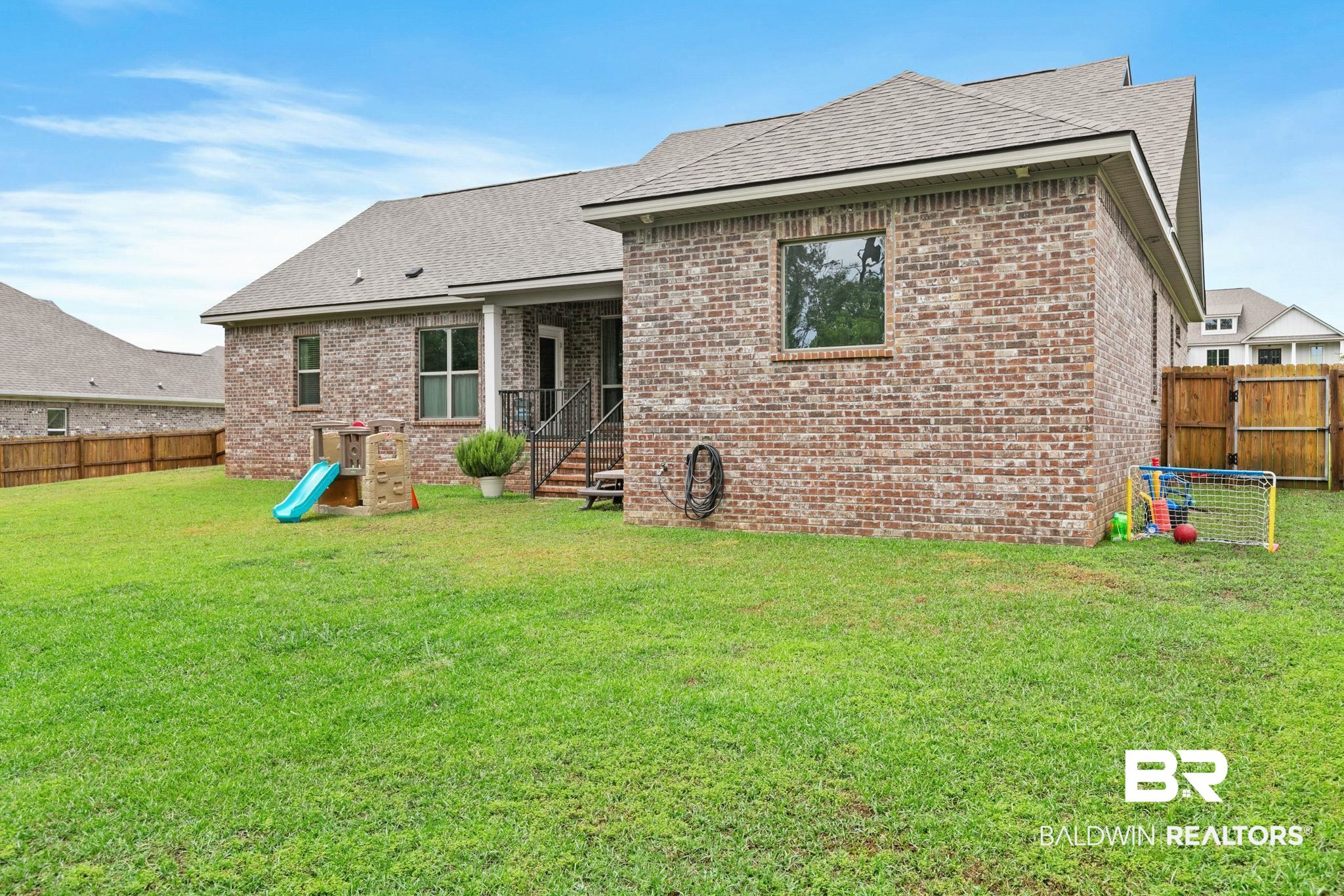 13233 Ibis Boulevard Daphne, AL 36527 - Photo 57 of 100 Expansive rear yard featuring a privacy fence, brick exterior with multiple windows, and a covered patio area with steps