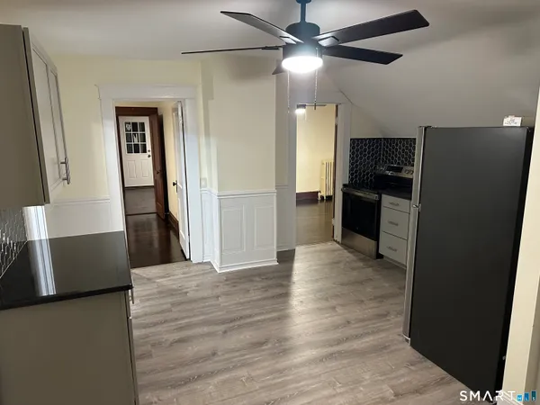a view of a refrigerator in kitchen and an empty room with wooden floor