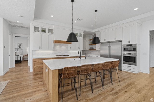 2278 Tawny Ridge Circle St. George, UT 84790 - Photo 10 of 61 Spacious kitchen featuring a large central island with seating, light wood-finish flooring, white upper cabinetry, natural wood lower cabinetry, and stainless steel appliances.