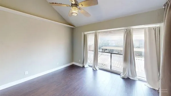 an empty room with wooden floor and windows with curtains