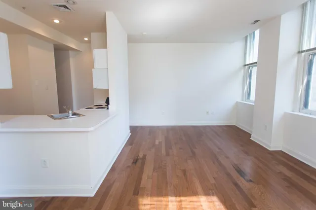 a view of a hallway to an empty room with wooden floor and a window