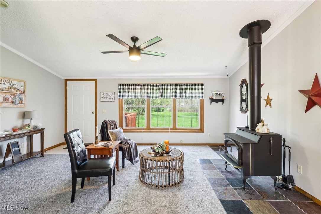 8307 Slagle Road Windham, OH 44288 - Photo 9 of 39 Living room with a wood stove, ceiling fan, baseboards, ornamental molding, and a textured ceiling